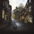By'Eck Its An Uphill Struggle shows a Yorkshire man pushing a bike up Haworth Main Street cobbles landscape art print by Danny Abrahams 