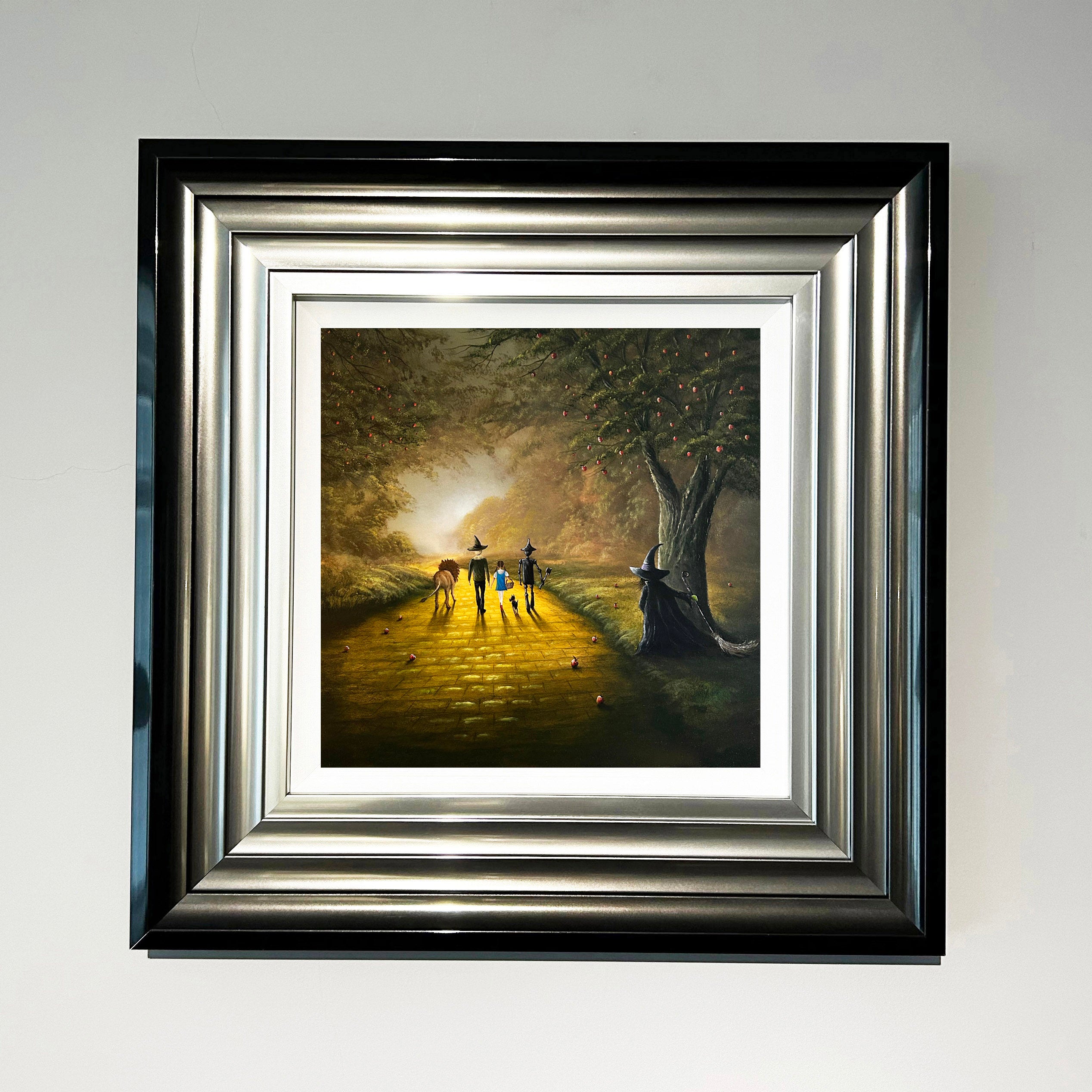 Wizard of Oz inspired landscape painting with Dorothy, Toto, tin man, scarecrow and lion walking the yellow brick road whilst the wicked witch watches from behind a tree by Danny Abrahams Art. 