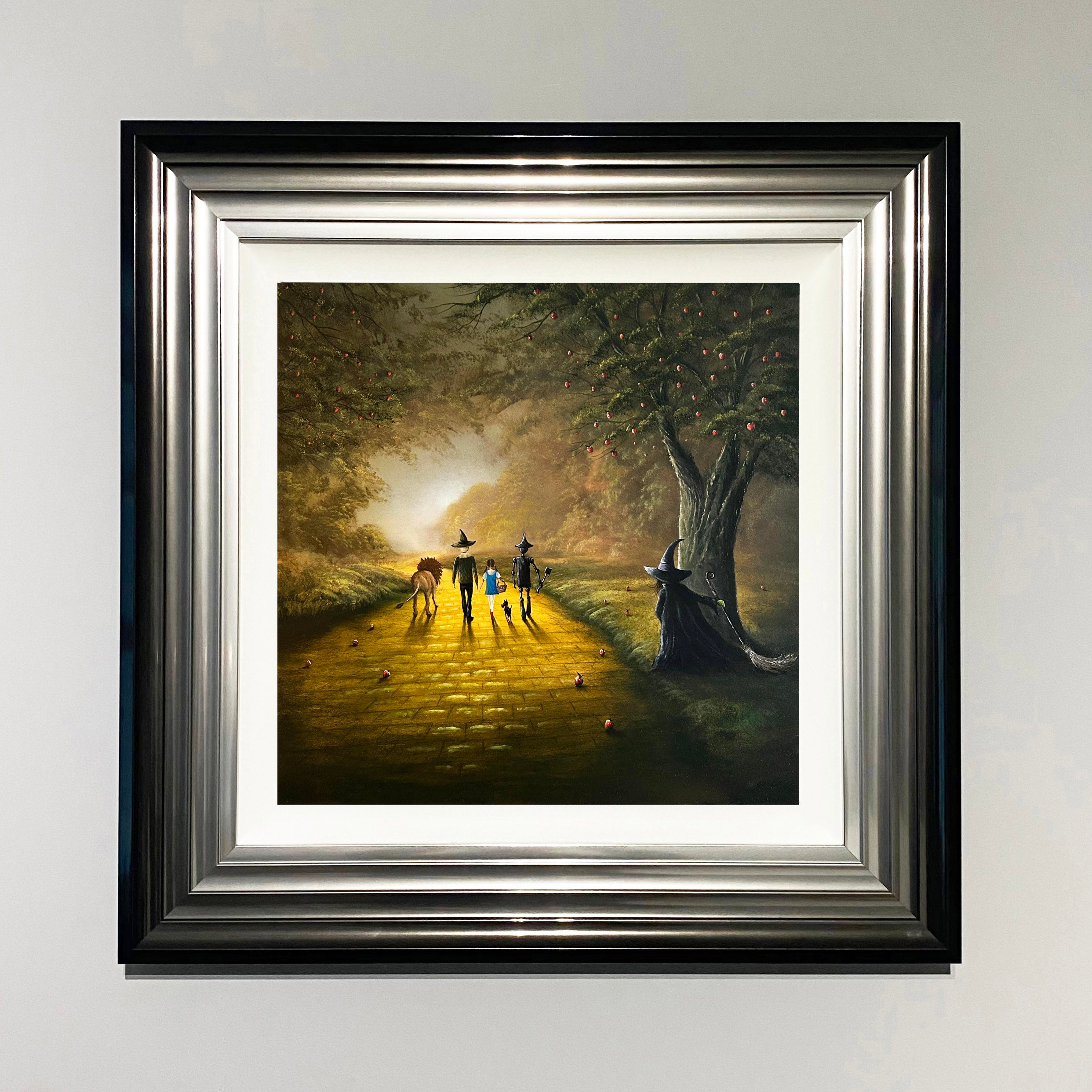 Wizard of Oz inspired landscape painting with Dorothy, Toto, tin man, scarecrow and lion walking the yellow brick road whilst the wicked witch watches from behind a tree by Danny Abrahams Art. 
